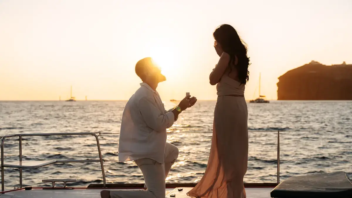 A marriage proposal on the catamaran's foredeck at sunset in the caldera