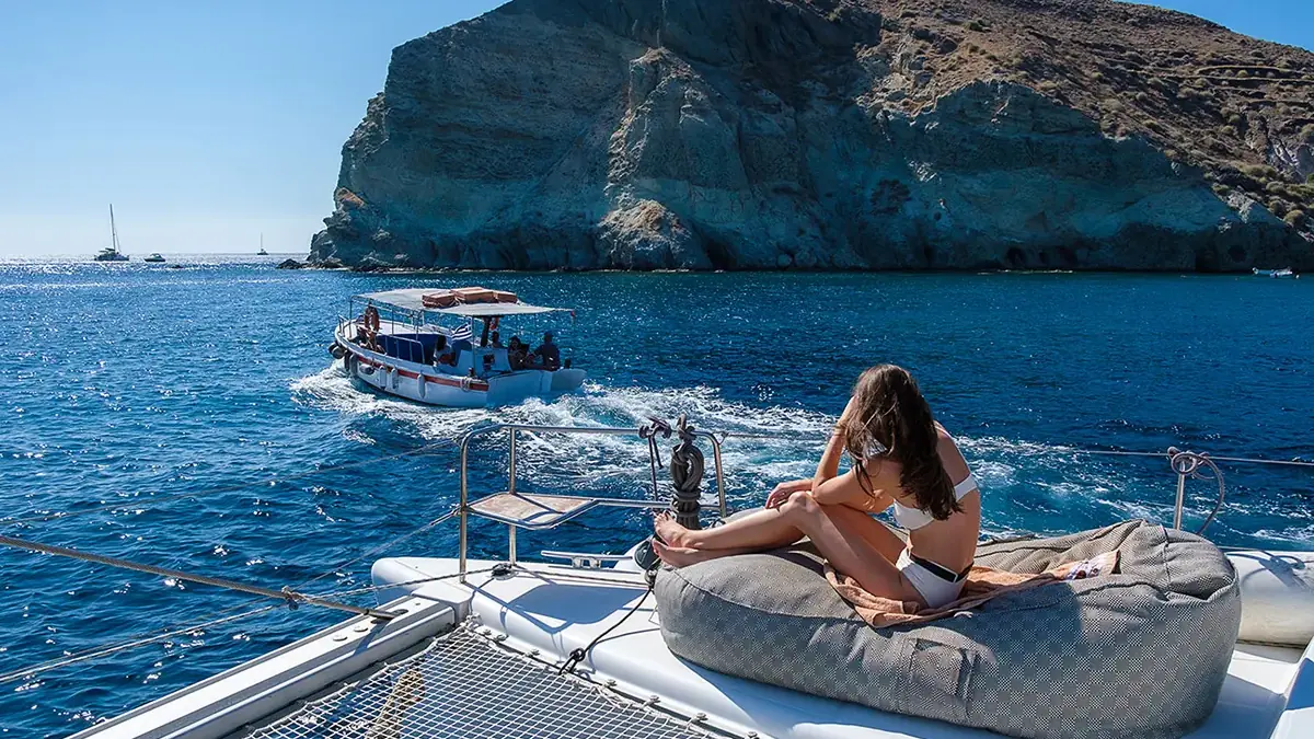 Guest relaxing on the bow beanbag as the catamaran cruises the Santorini caldera on a full-day charter