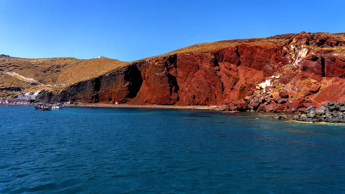 Red Beach Santorini from the water — rust-red volcanic cliffs above turquoise sea