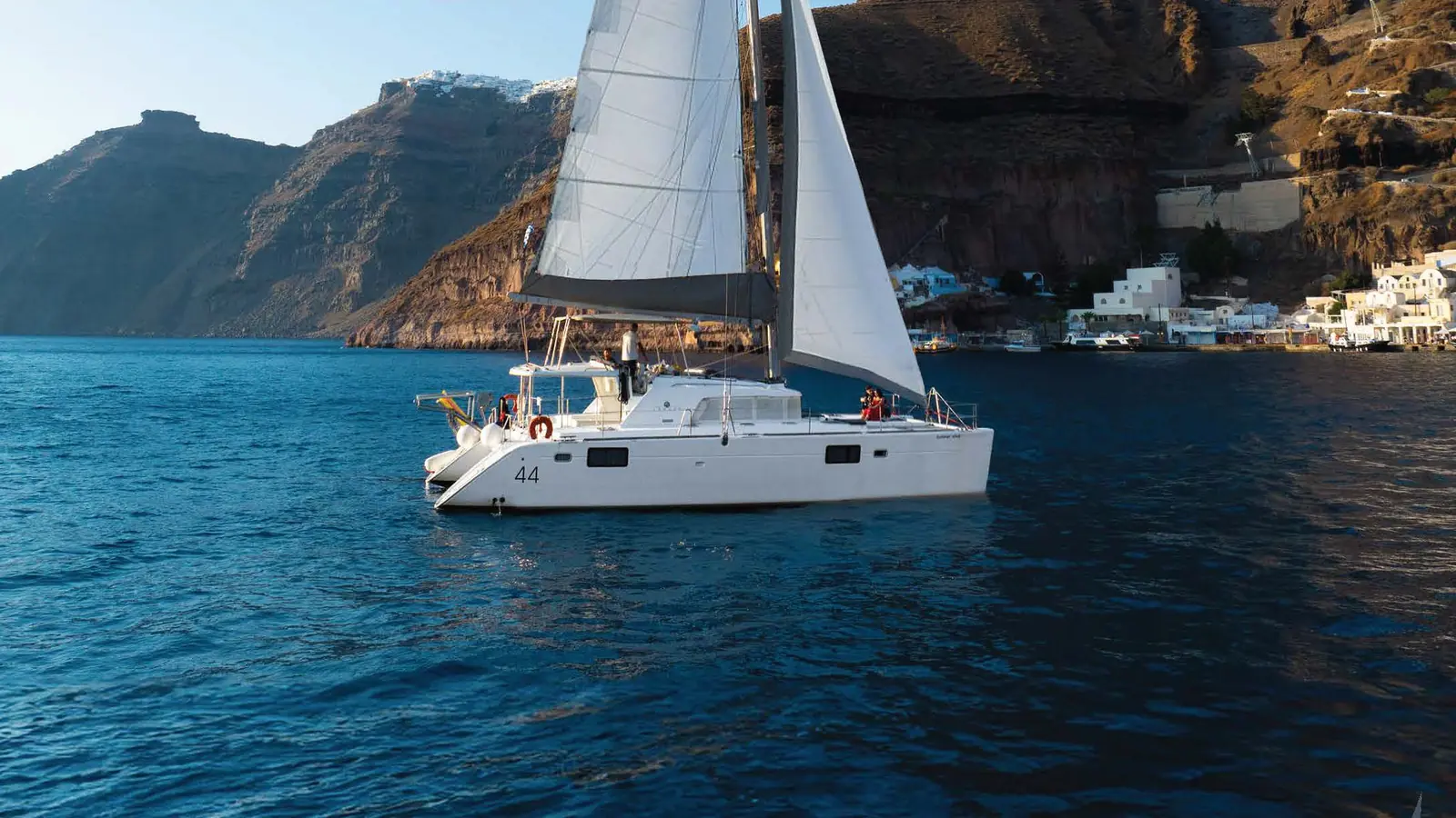Our Lagoon catamaran under sail below the caldera cliffs by Fira's old port, Santorini