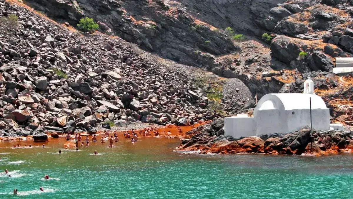 Swimmers in the warm rust-tinted bay of the Palea Kameni hot springs, Santorini
