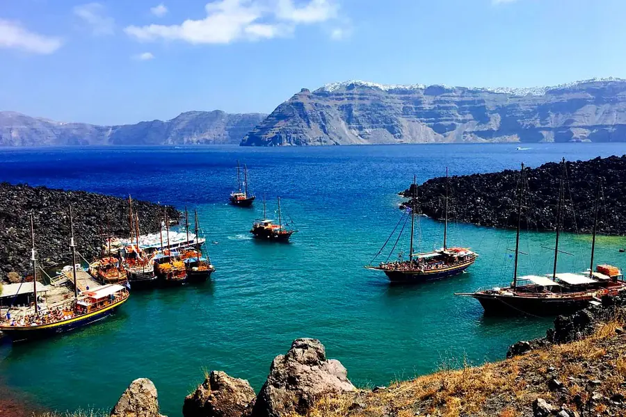 Boats moored at the volcanic islet of Nea Kameni with the caldera cliffs of Fira behind