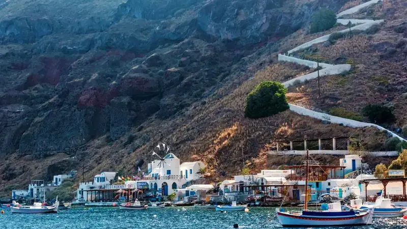 Thirasia's little port of Korfos with tavernas and a windmill under the cliff