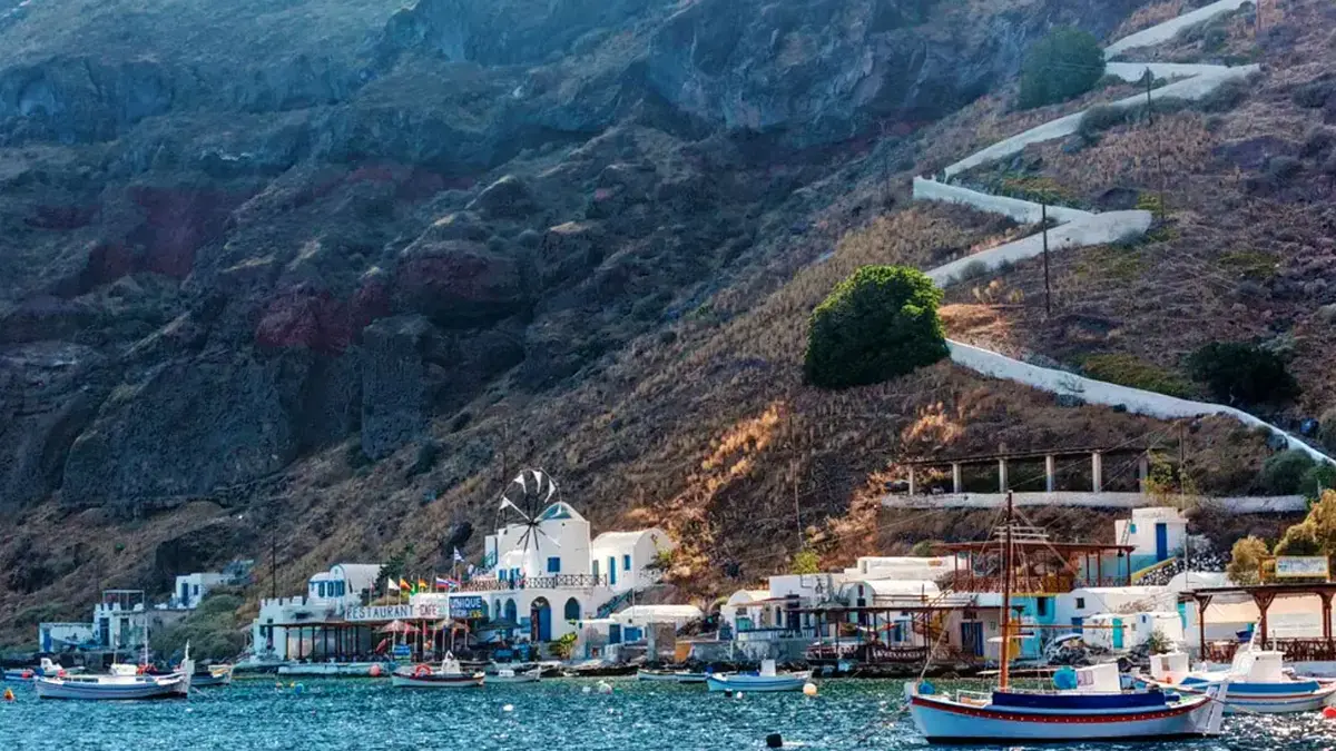 Thirasia's little port of Korfos — whitewashed tavernas and a windmill under the cliff, fishing boats on the water